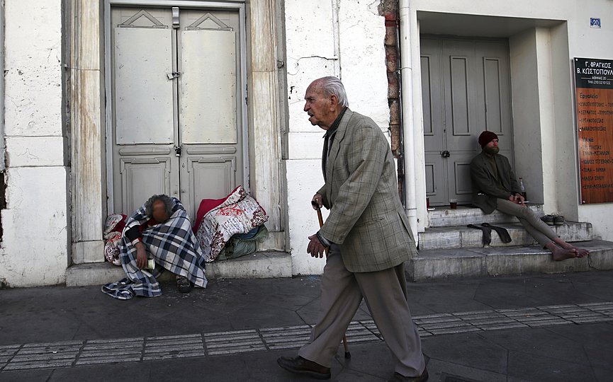 FILE - An elderly man passes by homeless men in Athens. (AP Photo/Thanassis Stavrakis)