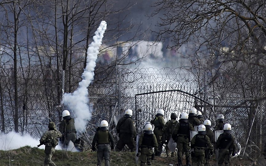 File- Greek police guard as migrants gather at a border fence on the Turkish side, during clashes at the Greek-Turkish border in Kastanies, Evros region, on Saturday, March 7, 2020. (AP Photo/Giannis Papanikos)