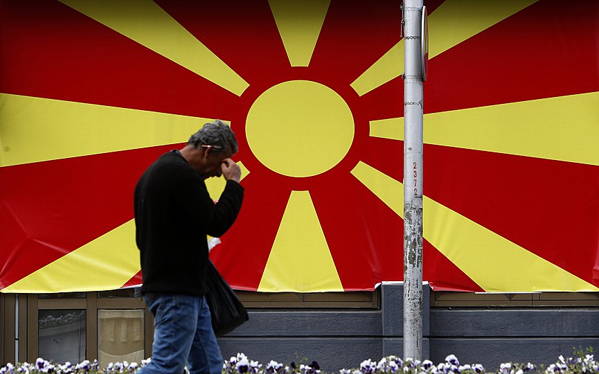 File- A man walks past the national flag set in a street in Skopje, North Macedonia. (AP Photo/Boris Grdanoski)