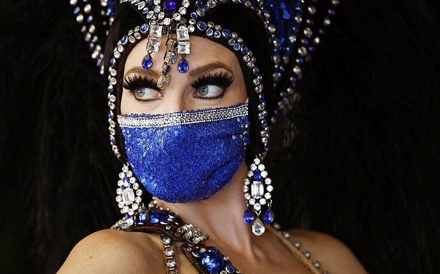 A showgirl in a face mask stands by the door at the reopening of Bally s Las Vegas hotel and casino, Thursday, July 23, 2020, in Las Vegas. (AP Photo/John Locher)