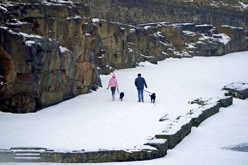 People walk with dogs after more snow fell overnight near Cullercoats on the north east coast of England, Friday Feb. 12, 2021. (Owen Humphreys/PA via AP)