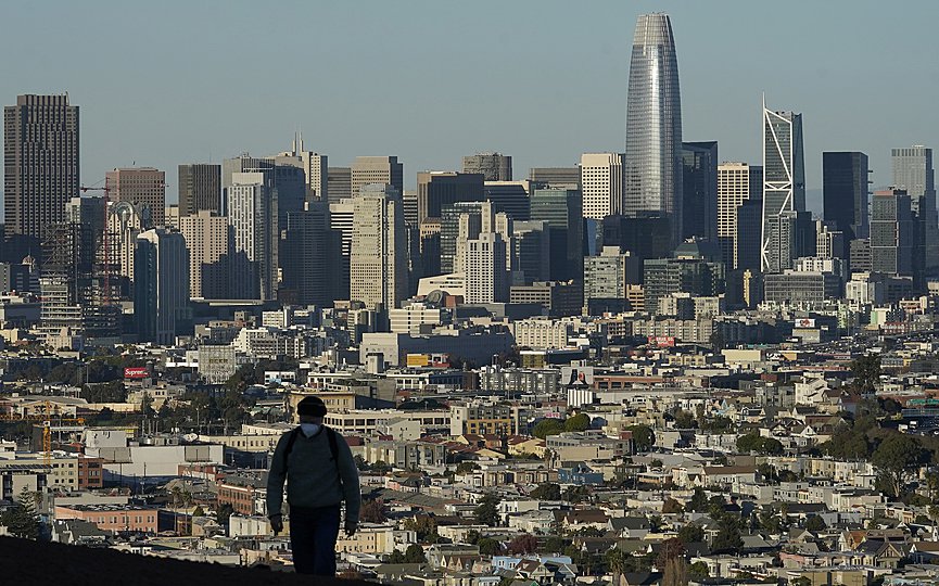 FILE - In this Dec. 7, 2020, file photo, a person wearing a protective mask walks in front of the skyline on Bernal Heights Hill during the coronavirus pandemic in San Francisco. (AP Photo/Jeff Chiu, File)