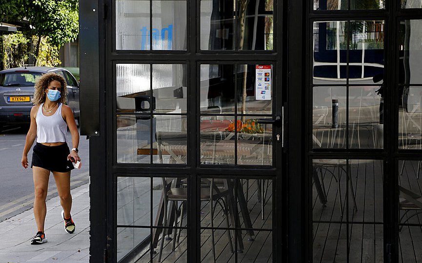 A woman wearing protective face mask walks outside of a closed cafe amid COVID-19 pandemic restrictions government in central capital Nicosia, Cyprus, Thursday, May 6, 2021. (AP Photo/Petros Karadjias)